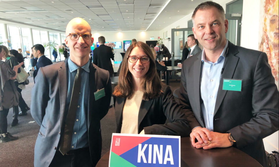 Tre personer står i en konferenslokal