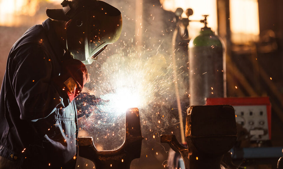 Bild på en svetsare i skyddsutrustning som arbetar med intensivt gnistande svetslåga