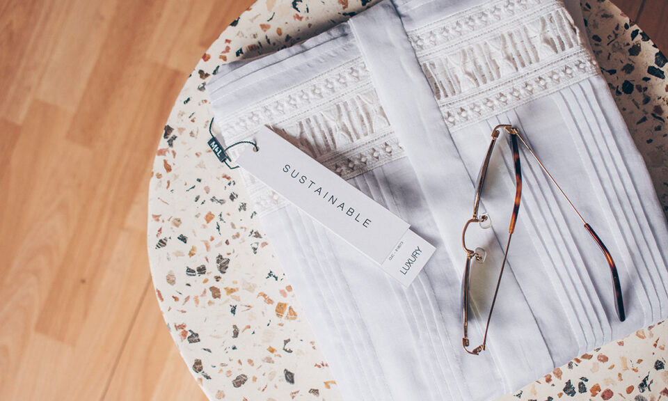 Bild på vikta hållbara kläder med etikett bredvid glasögon på ett bord