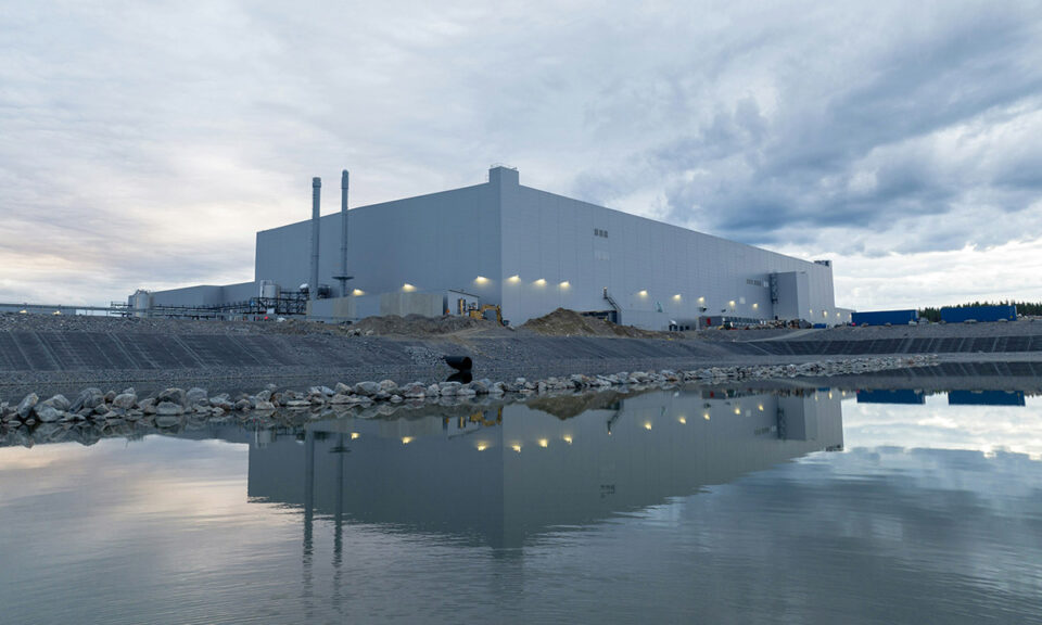 Bild på modern industribyggnad vid vatten, speglad i en stilla damm