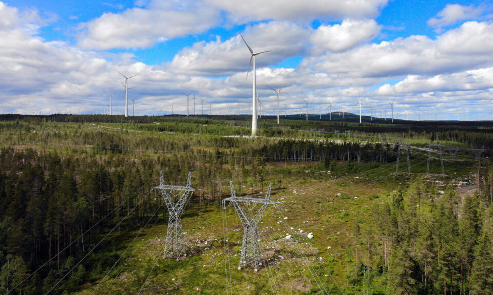Bilden visar vindkraftverk och elnät i Sverige. Vindkraftverken och ledningsgatan är omgärdad av skog. Himlen är blå med vita moln.