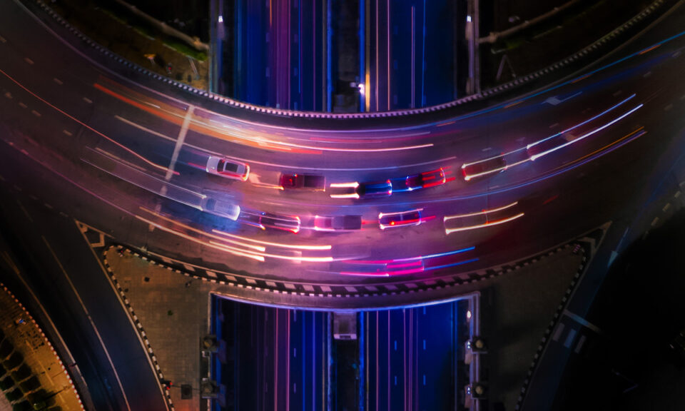 Flygfoto av tät stadstrafik nattetid med ljusspår från bilar på en upplyst motorvägskorsning